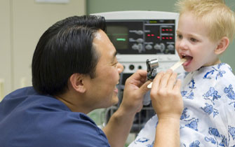 Pediatrician examining child's throat in clinic