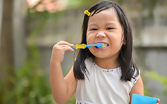 Girl brushing teeth with blue toothbrush outdoors.