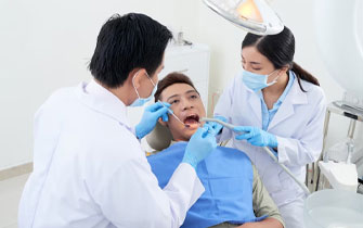 Dentist examining patient's teeth with assistant.